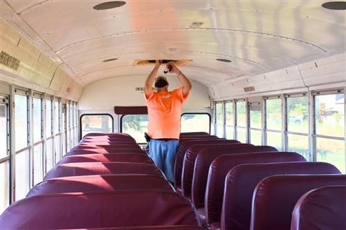 driver in bus amid rows of seats inspecting the roof vent 